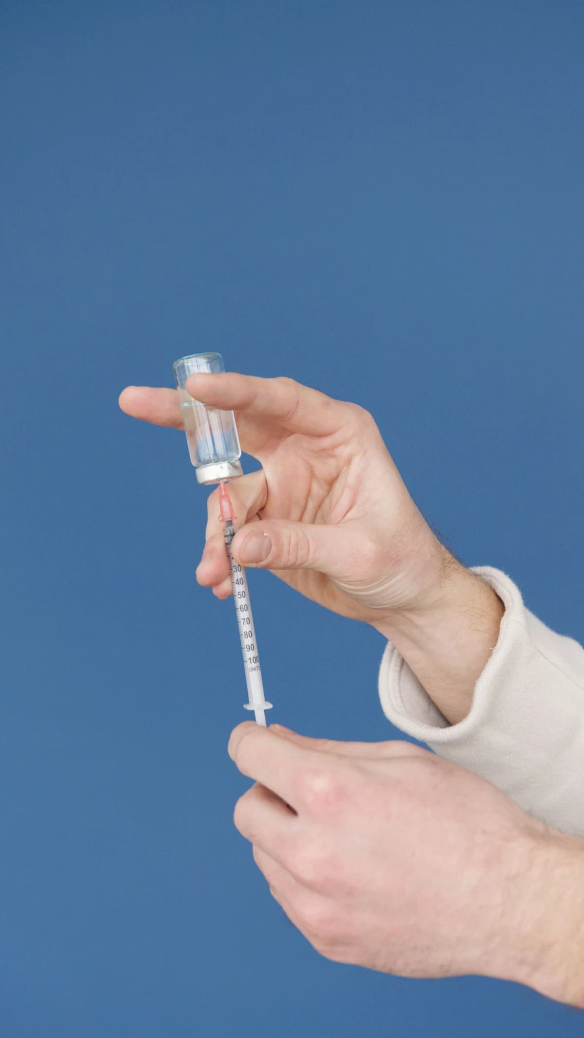 Close-up of hands filling a syringe with vaccine from a vial