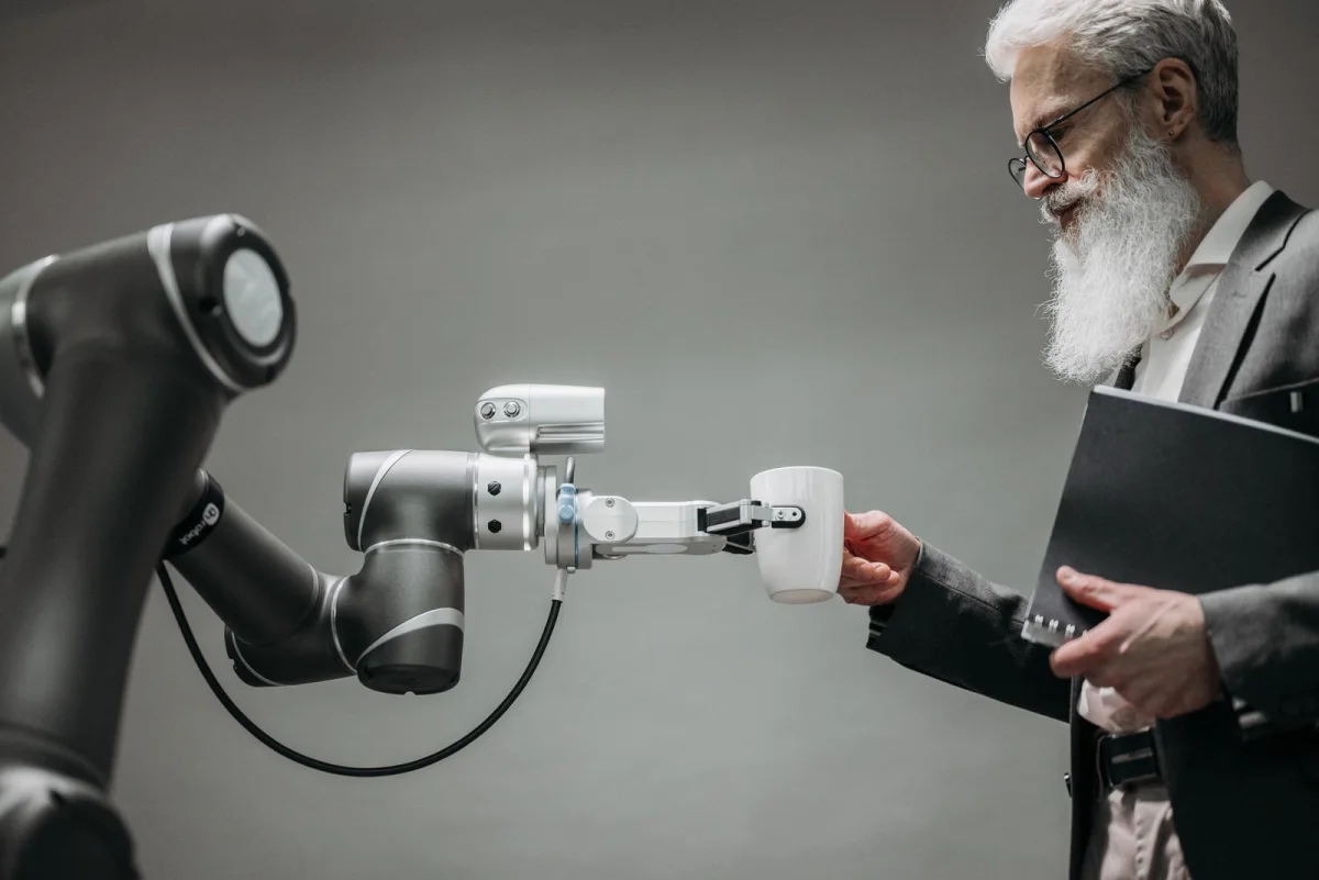 An elderly man receives a cup from a robotic arm in a modern office, symbolizing autonomous AI agents working inside businesses
