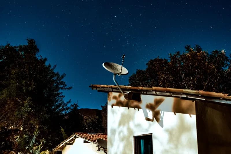 A satellite dish on a rural house roof under a starry night sky