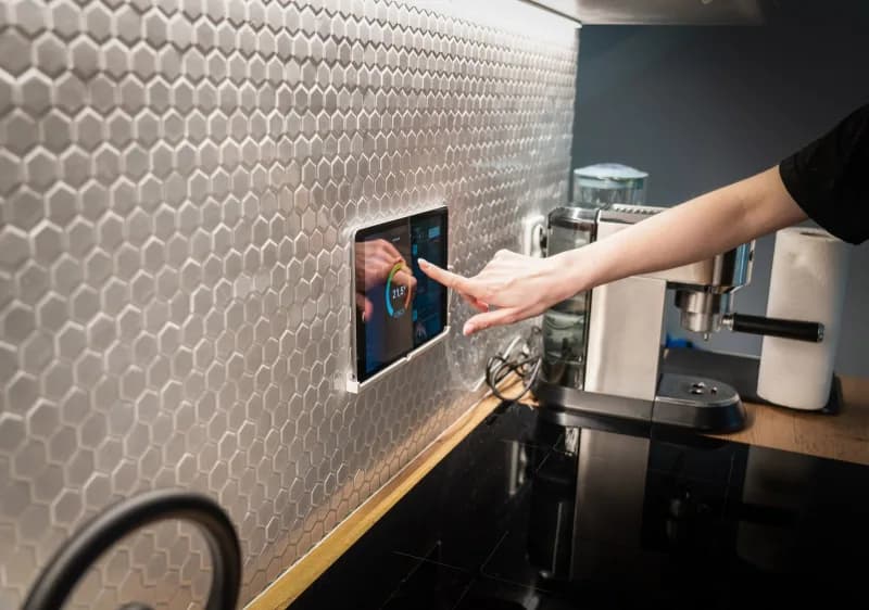 A smart home touchscreen control panel mounted on a wall