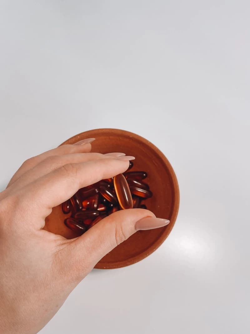 A hand holding vitamin supplement pills over a small bowl