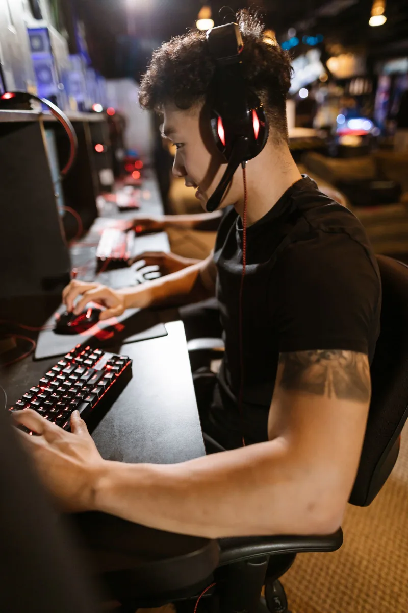 A gamer wearing headphones focused on a computer in a cyber-themed esports setting
