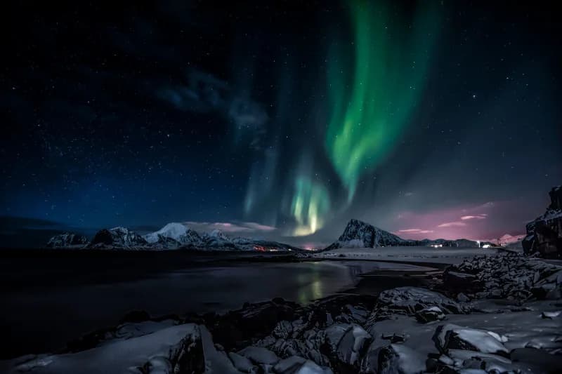 Green aurora borealis curtains over snow-covered mountains under a starry night sky