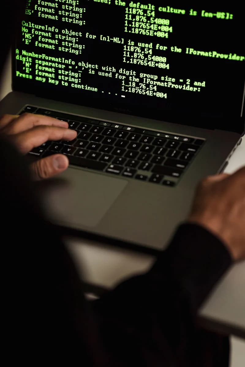 Close-up of a hacker's hands typing on a laptop in a dark room, representing AI-powered phishing attacks