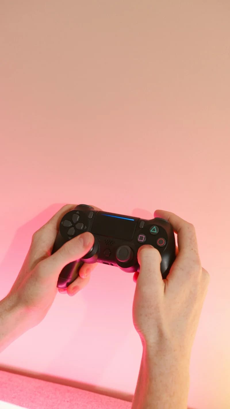 A person holding a wireless game controller against a pink background